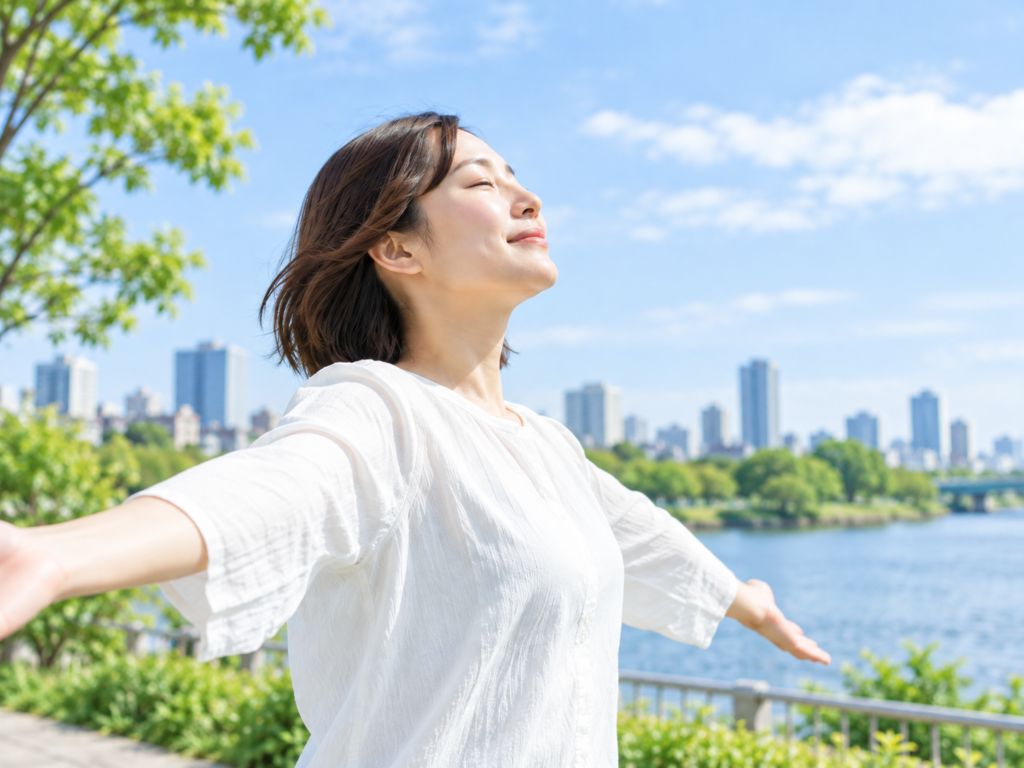青空の下、水辺の公園で両手を広げて深呼吸をする女性